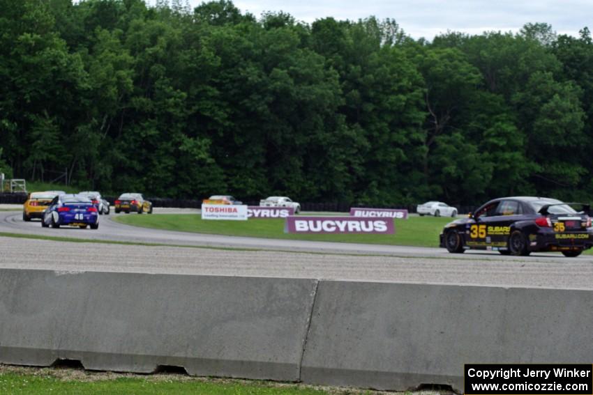 The field follows the pace car through the carousel during an early yellow.