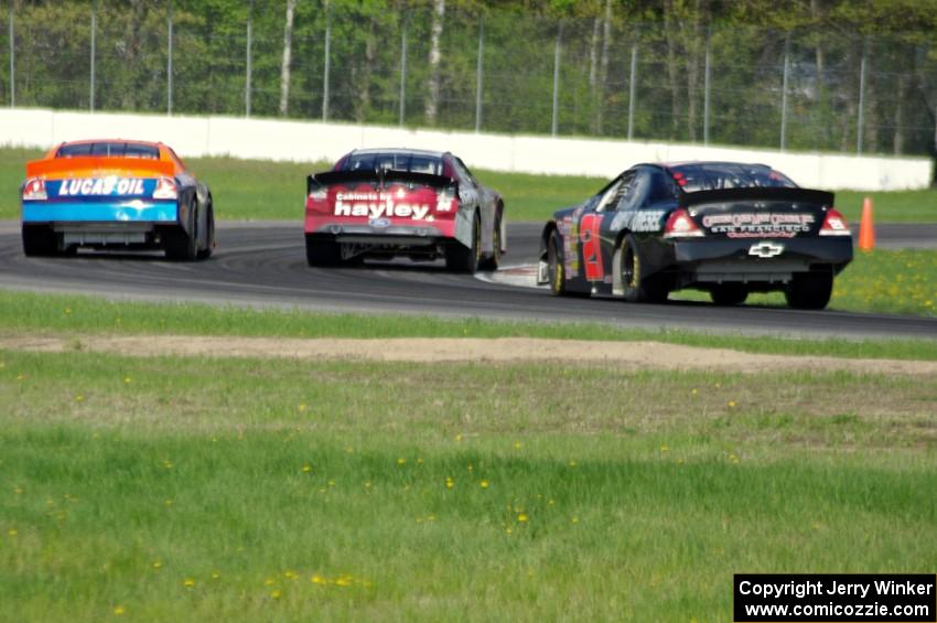 Cameron Hayley's Ford Fusion passes Derek Thorn's Ford Fusion while Michael Self's Chevy Impala follows.