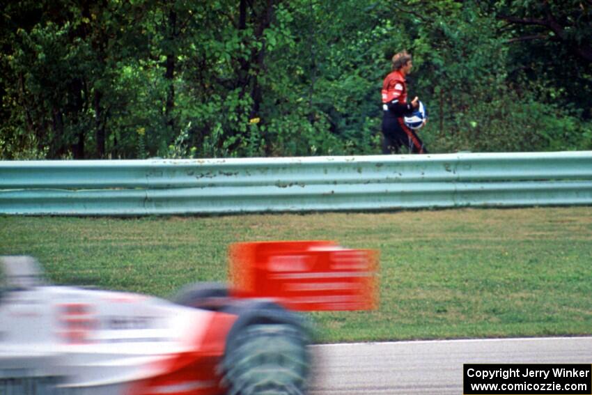 Eddie Cheever walks back to the pits as Emerson Fittipaldi's Penske PC-21/Chevy passes by.