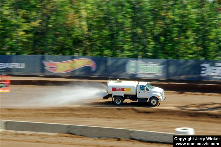 A water truck sprays down the track surface.