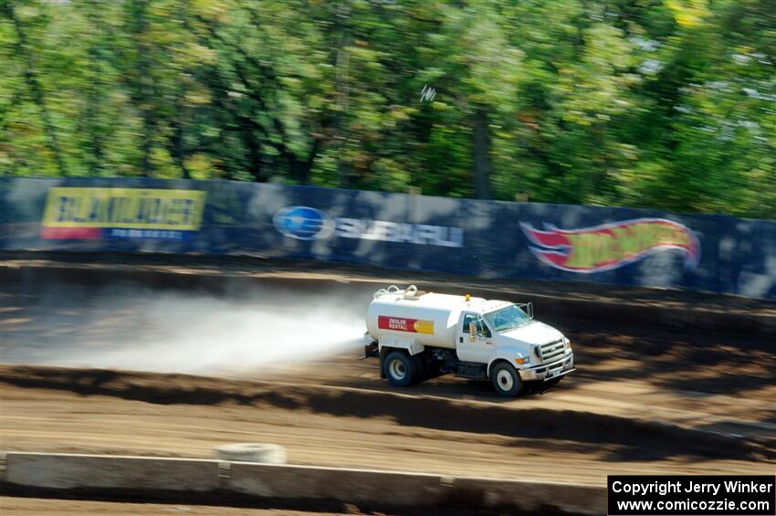 A water truck sprays down the track surface.