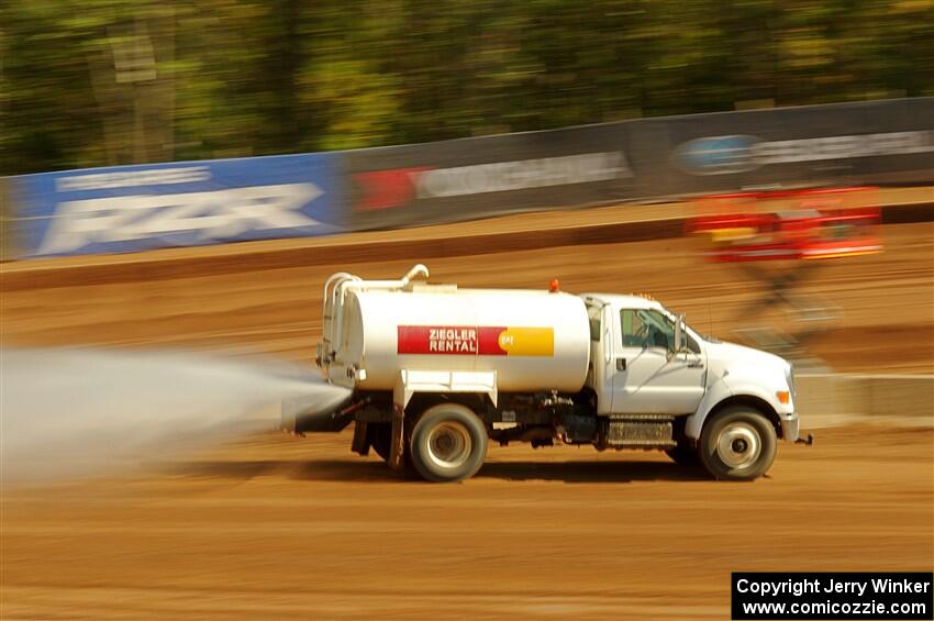 A water truck sprays down the track surface.