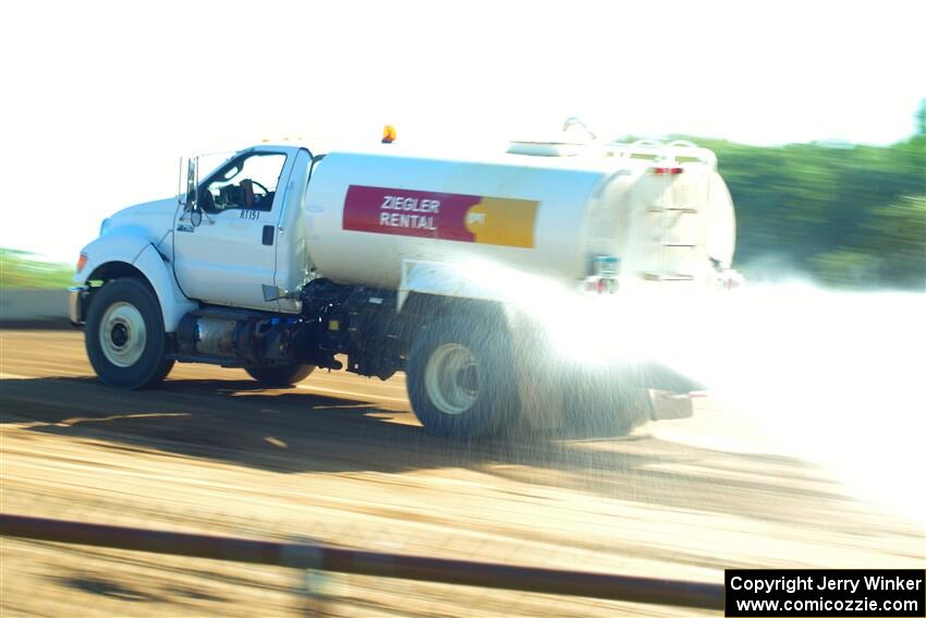 A water truck sprays down the track surface.