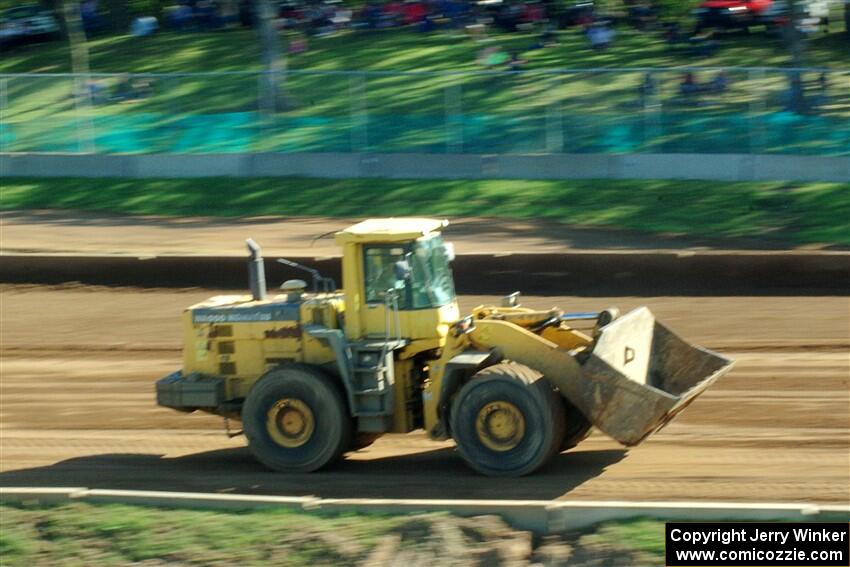 A front-end loader moves dirt to help smoothen out the track surface.