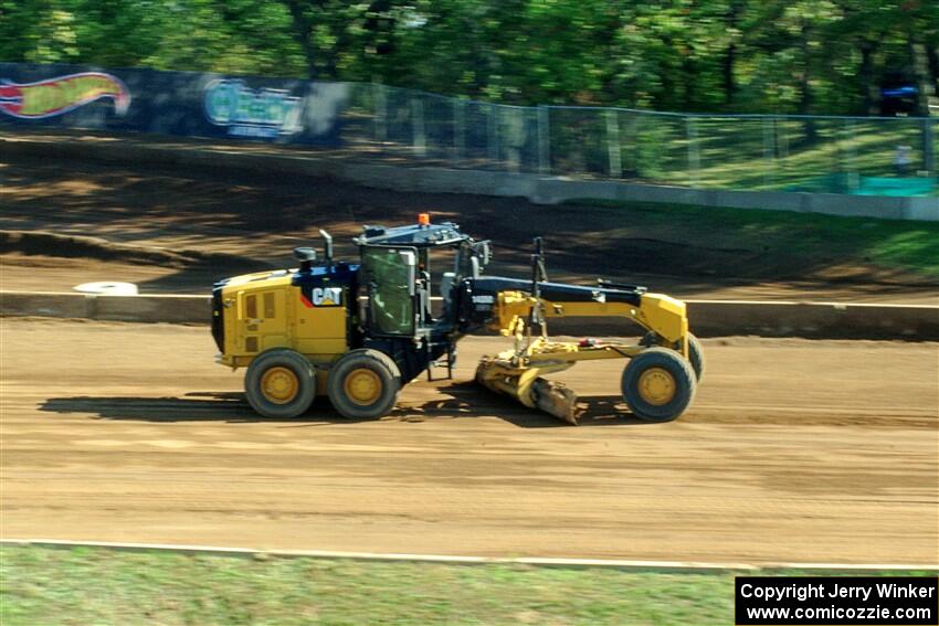 A road grader smooths out the track surface.