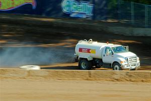 A water truck sprays down the track surface.