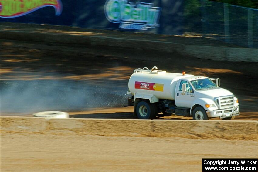 A water truck sprays down the track surface.