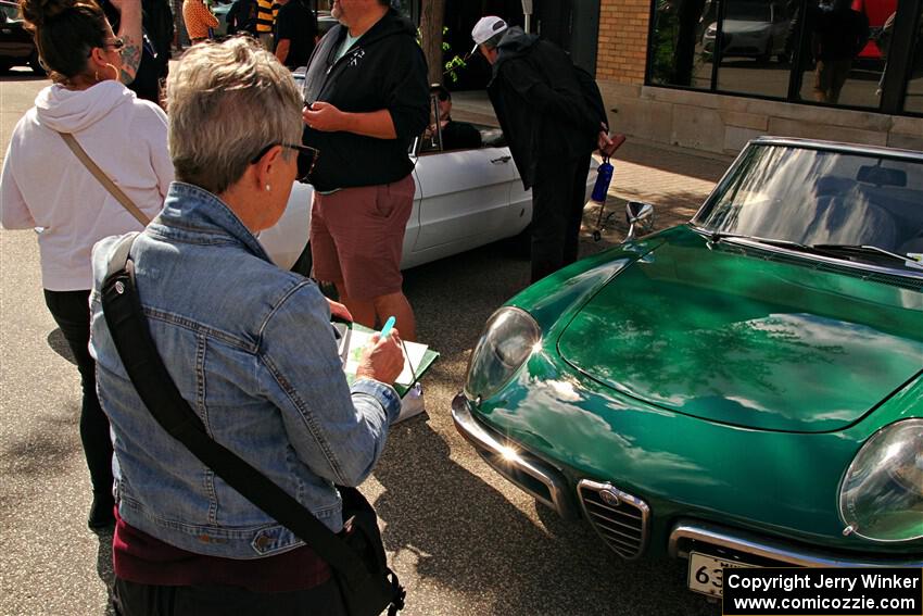 A woman paints a small picture of a Alfa Romeo Veloce Spider at the show.